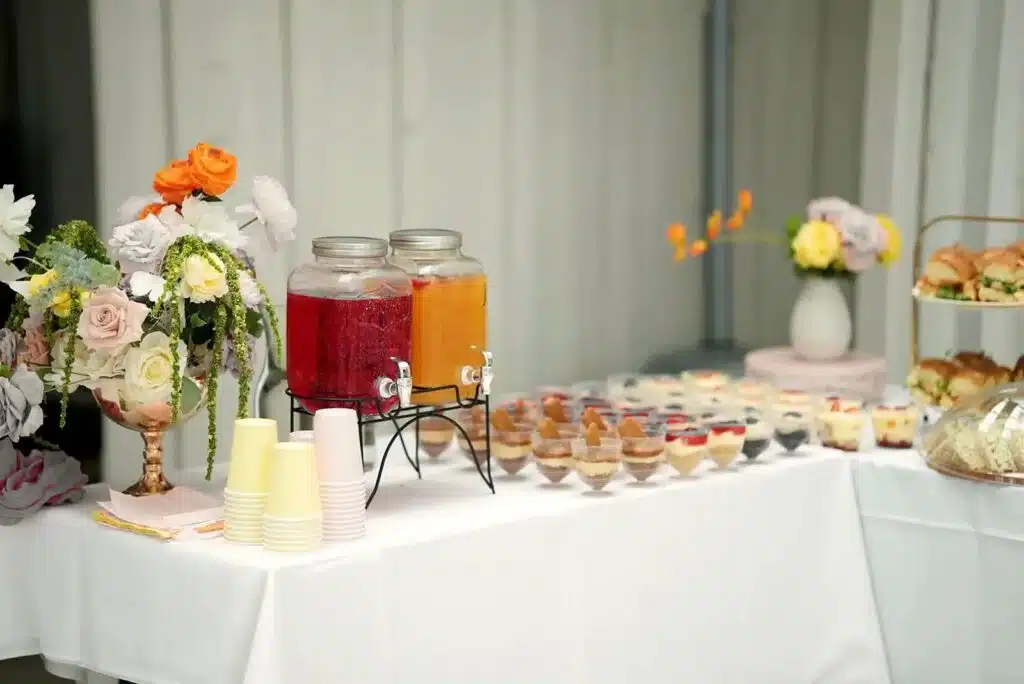 A drinks and dessert station with juice dispensers, flowers and dessert cups