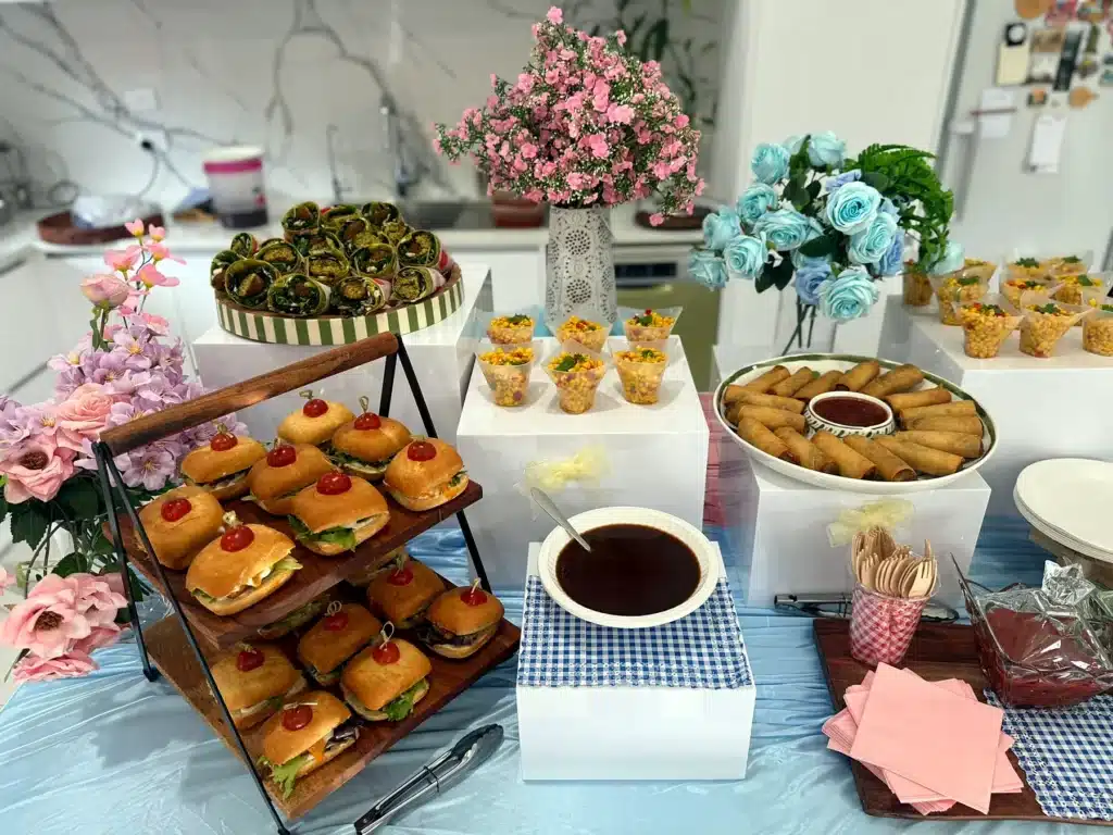 A party table with a slider tower, savoury cups, spring rolls and drinks