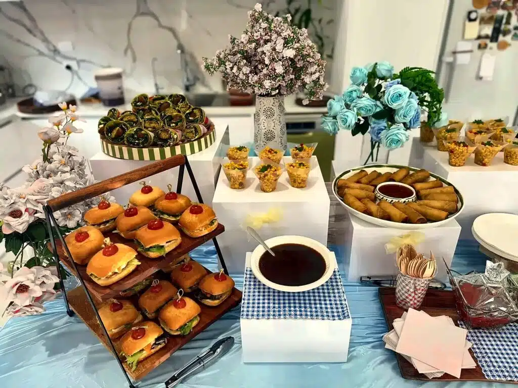 A party table with a slider tower, savoury cups, spring rolls and drinks